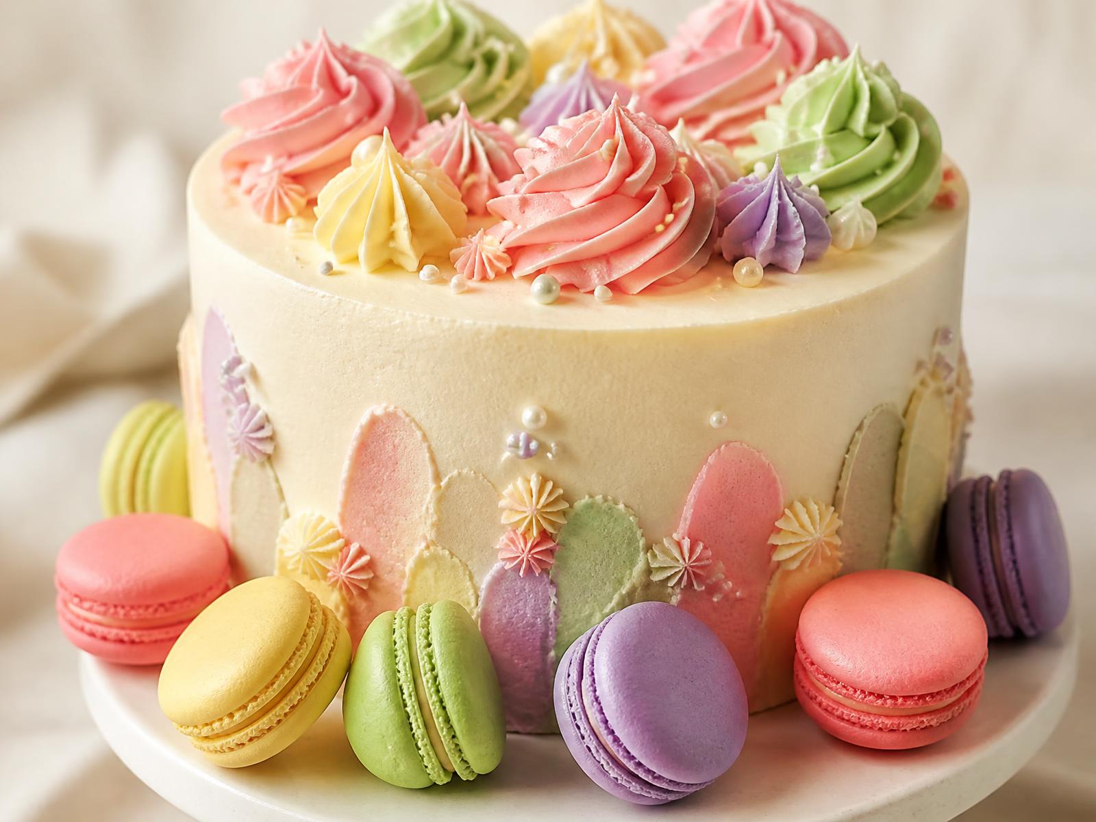 Pastel buttercream celebration cake surrounded by colourful macarons